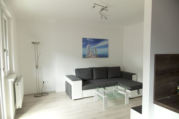 A modern living room with a grey sectional sofa, a glass coffee table, a painting of a pier on the wall, and a floor lamp.