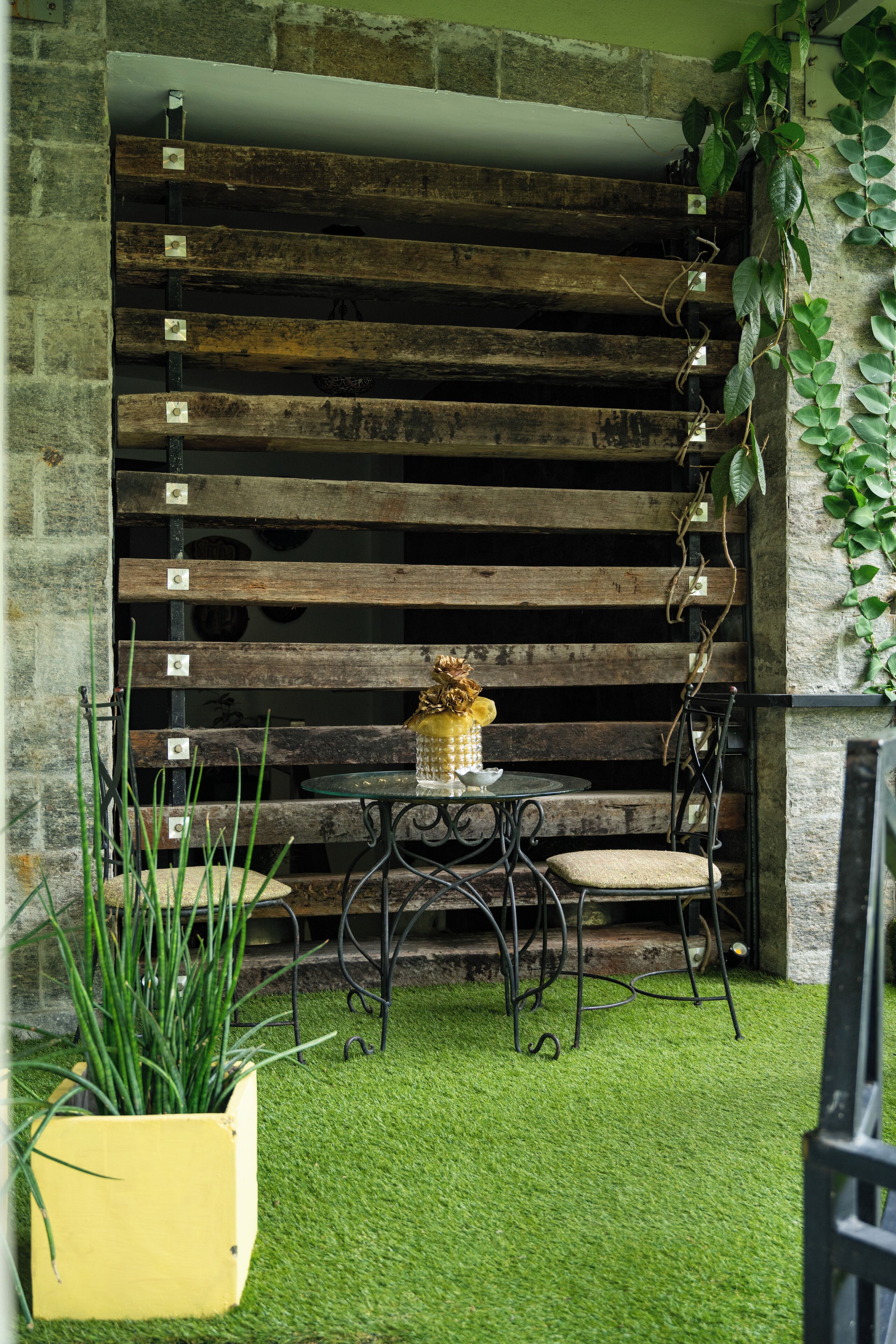 Un espace extérieur aménagé dans un style rustique, avec un mur en bois à lattes, une petite table ronde et des chaises.
