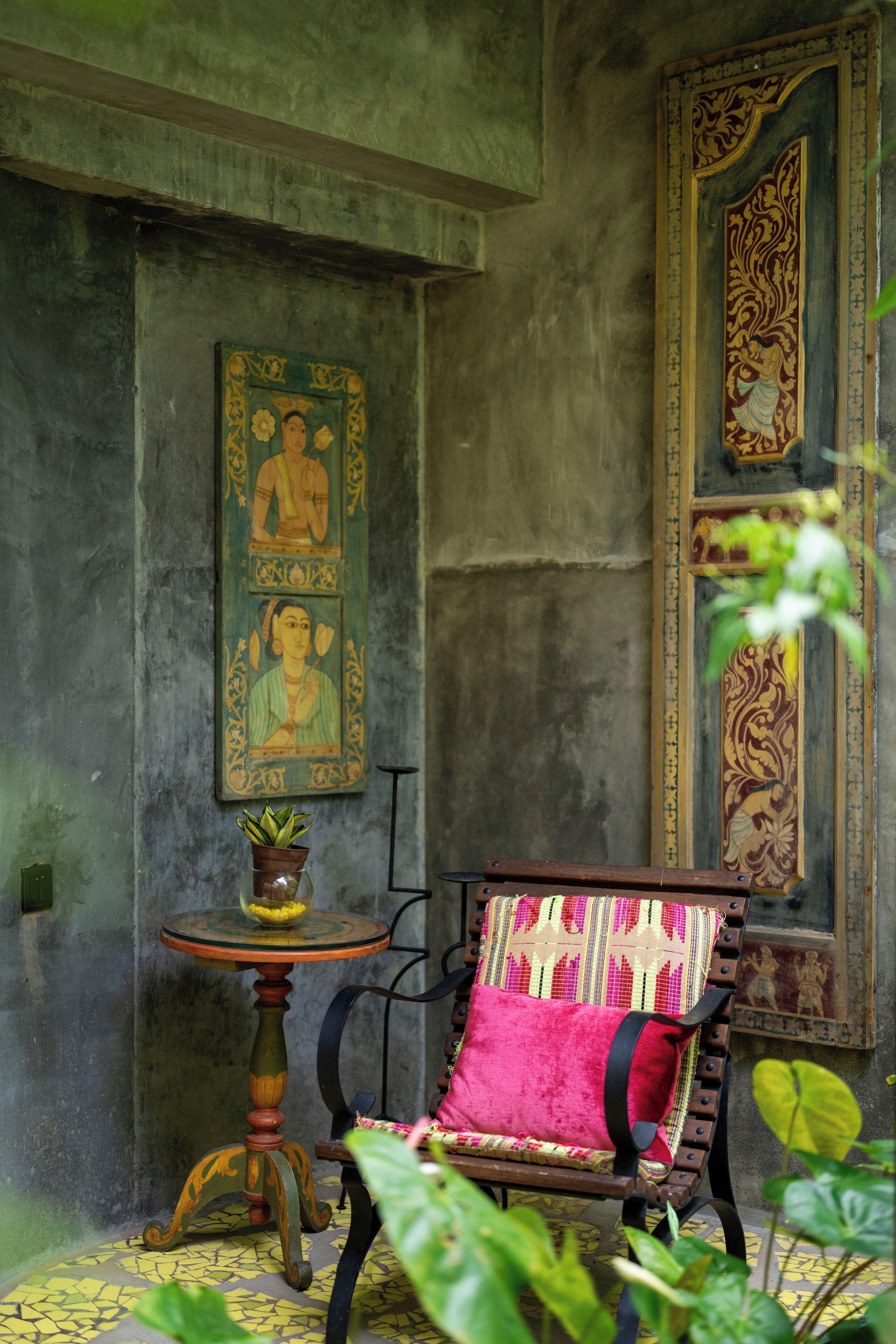 A room with a traditional chair, a small table with a plant, and two framed artworks on the walls.