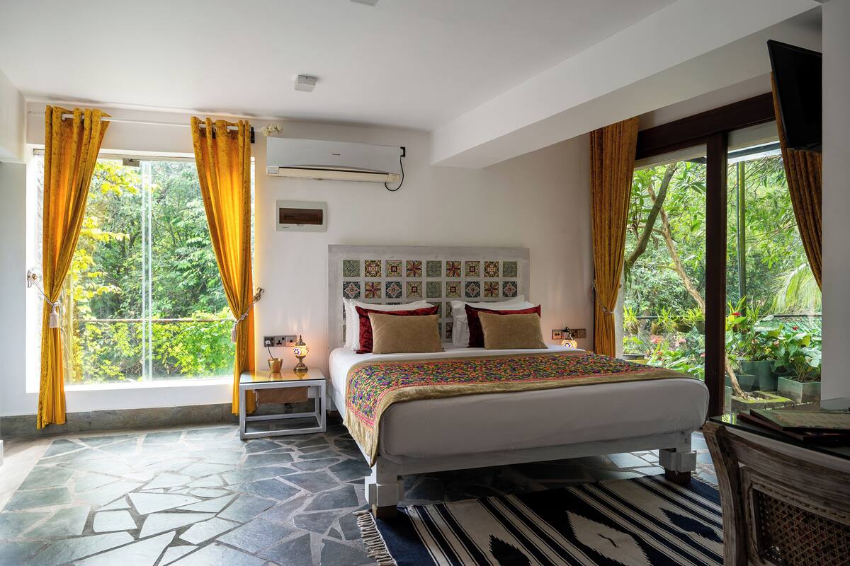 Une chambre à coucher avec un grand lit, une table de chevet, un climatiseur fixé au mur et une fenêtre avec des rideaux.