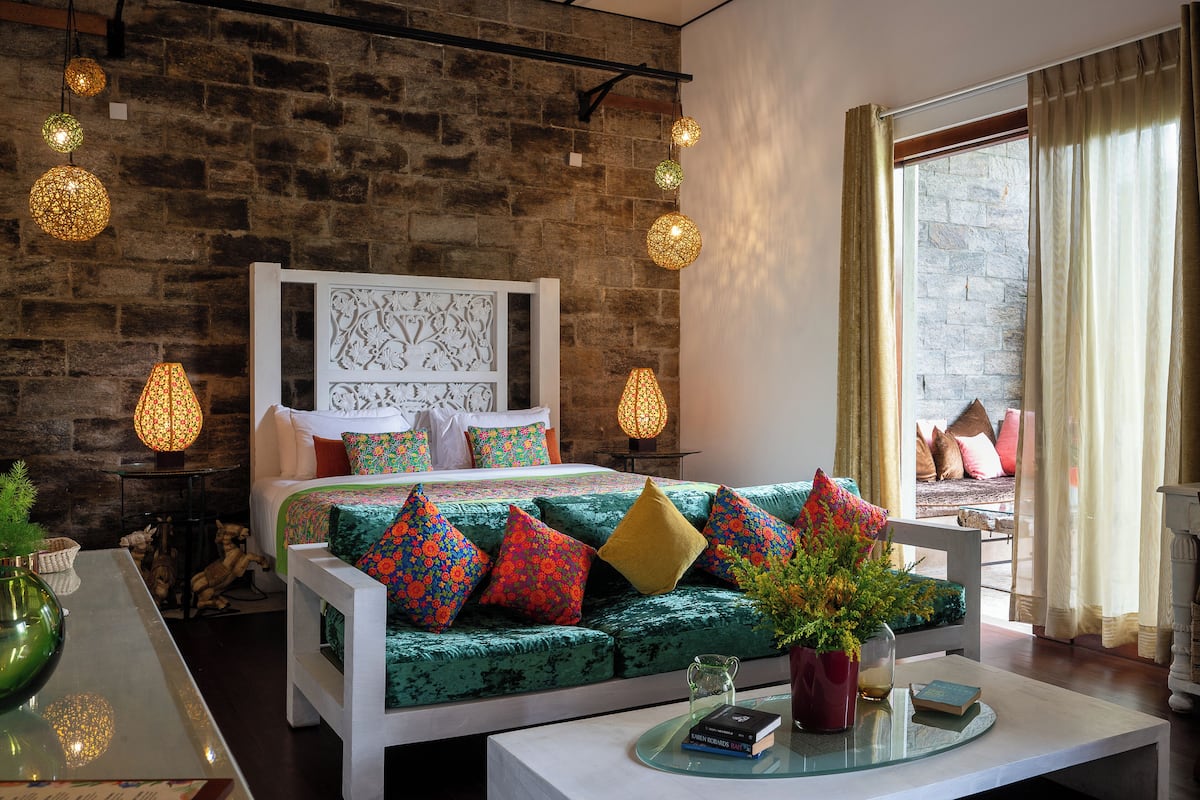 Une pièce chaleureuse avec un canapé vert, des coussins à motifs, un lit blanc et un mur en pierre.