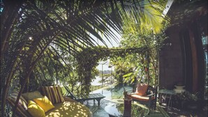 Un área de estar al aire libre con ambiente tropical, que incluye una hamaca, sillas acolchadas y una mesa redonda.