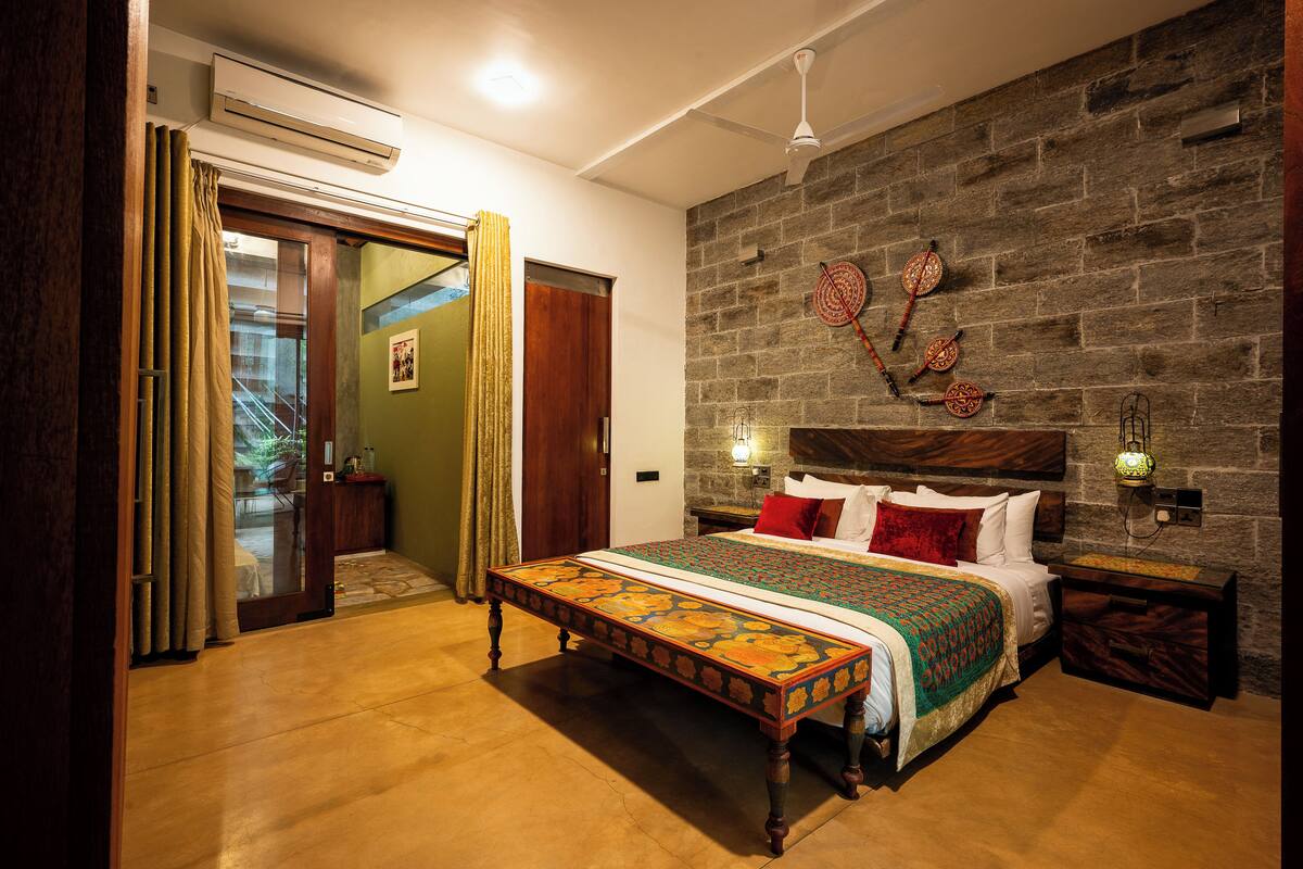Une chambre à coucher avec un grand lit, une tête de lit en bois, un mur en pierre et une petite table avec une lampe.