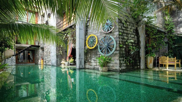 Un área de piscina con un muro de piedra, una banca de madera y una escalera que conduce a un nivel superior.