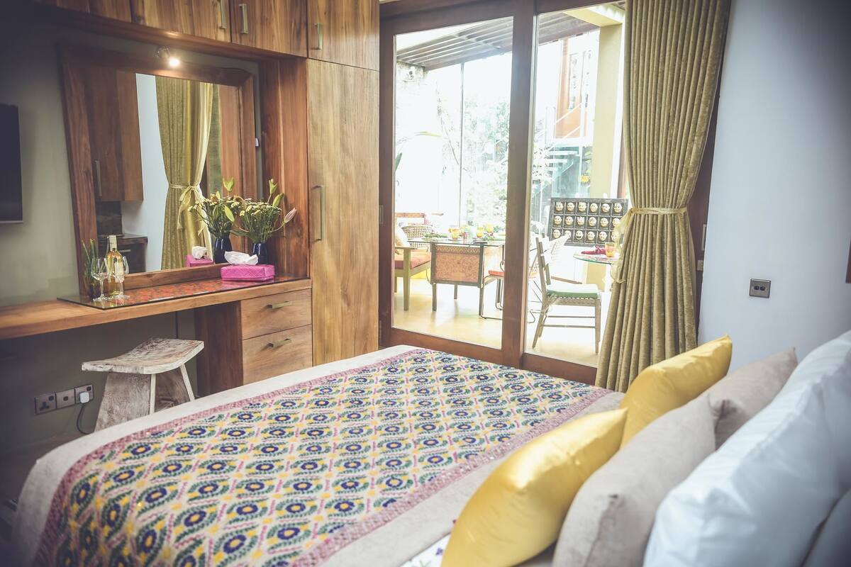 Une chambre avec un lit, un bureau en bois, un miroir et une vue sur une terrasse extérieure.