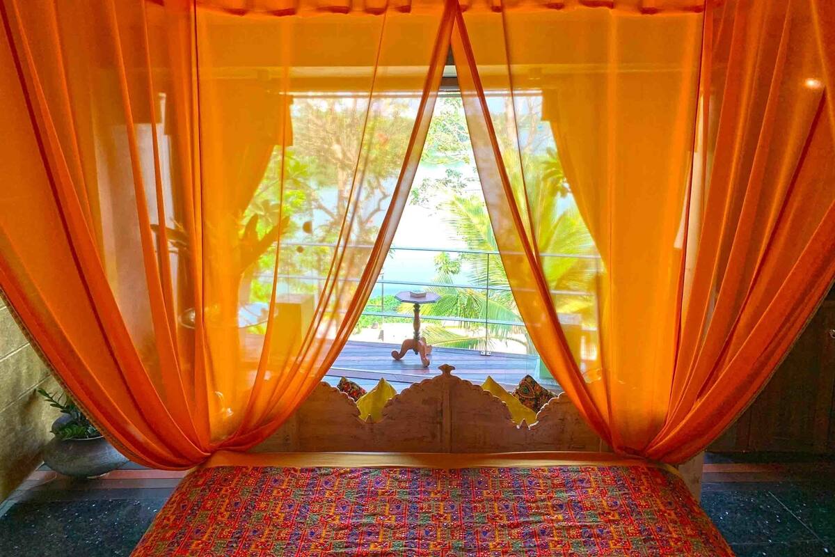 Une chambre avec un lit, des rideaux orange et une vue sur la verdure.