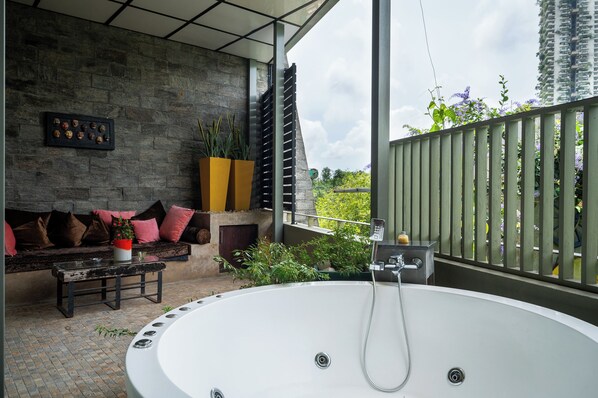 Un baño exterior moderno con una bañera grande, una pared de piedra y una zona de estar con cojines.