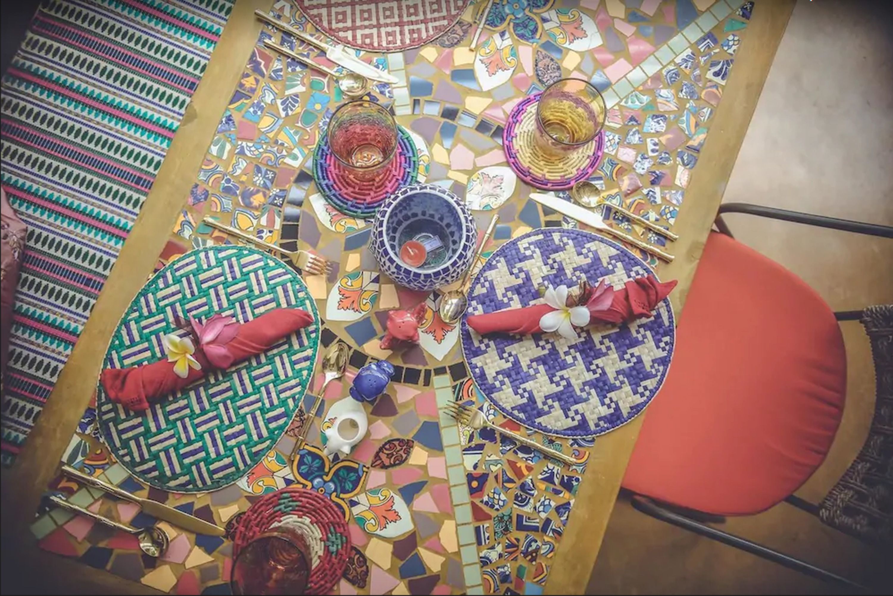 A dining table with colorful mosaic tiles, plates, napkins, and cutlery.