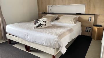 Un lit bien fait, avec une tête de lit à motifs, une table de chevet sur laquelle se trouve un téléphone et une prise électrique au mur.