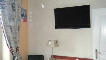 Habitación de hotel con televisión montada en la pared, escritorio con lámpara, una silla y una puerta.