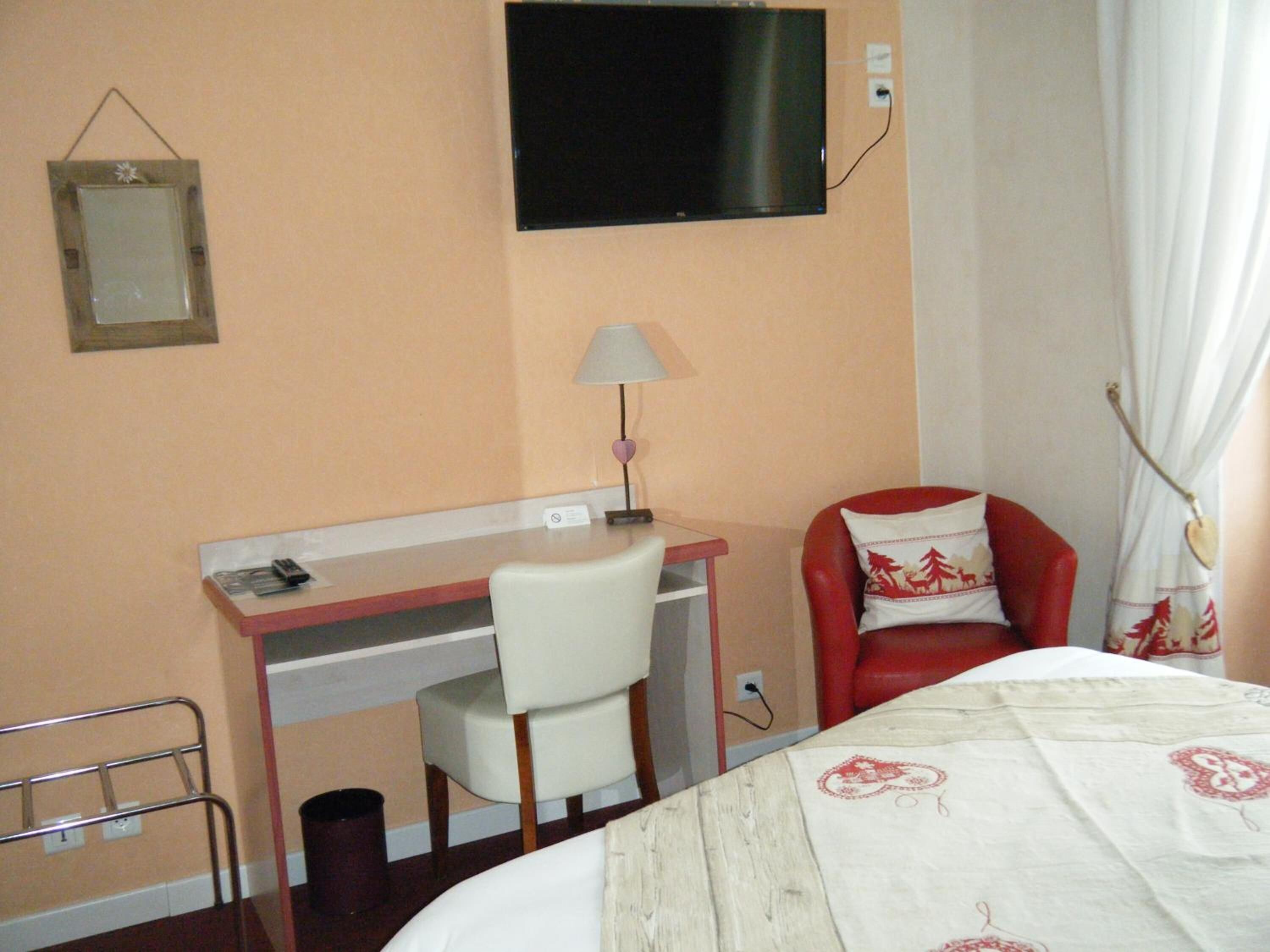 Quarto de hotel com uma escrivaninha, uma cadeira, uma cama, uma televisão e um abajur.