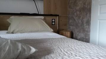A bed with a wooden headboard, a bedside table, and a wall-mounted light switch.