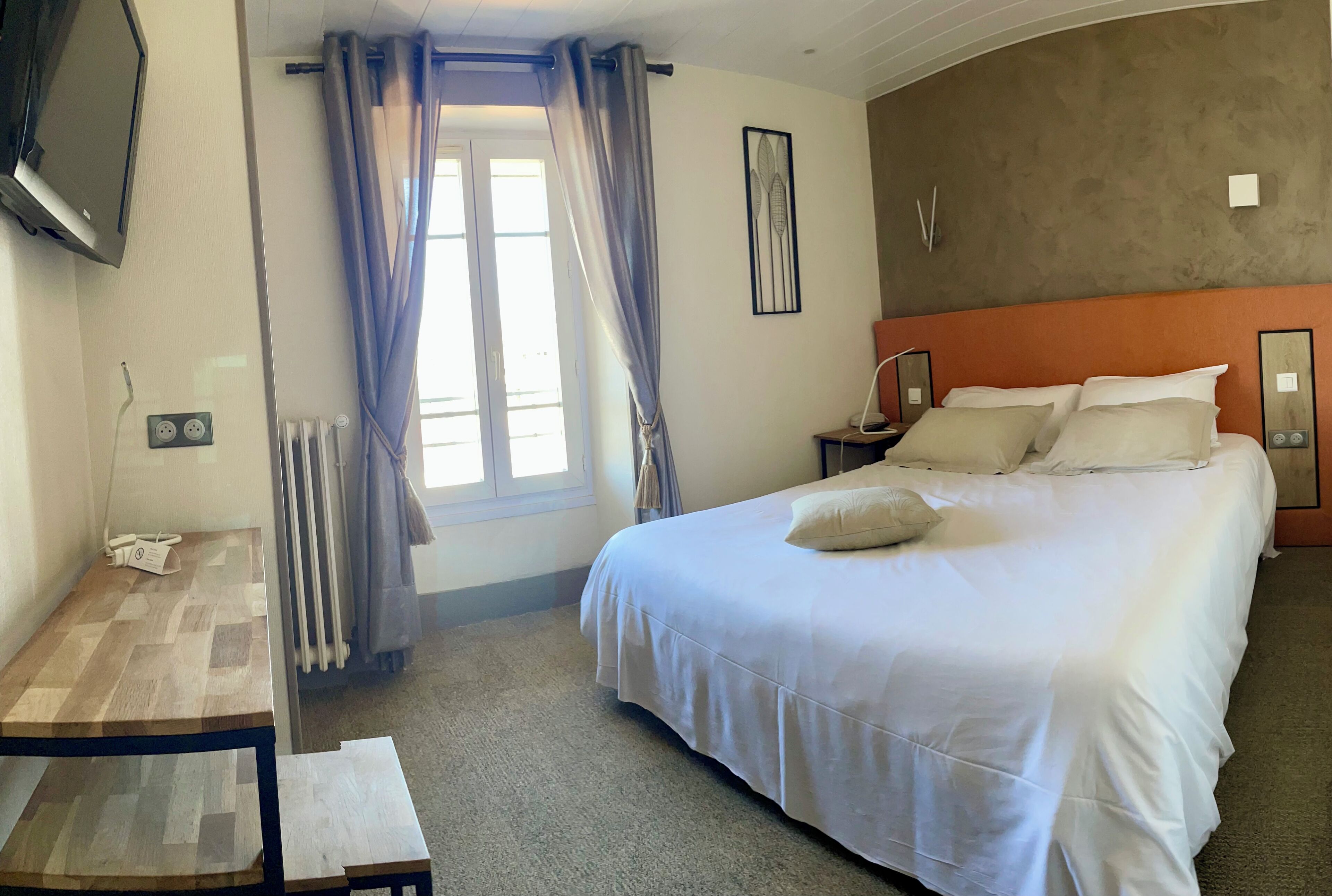 Una habitación de hotel con cama, mesita de noche y televisor montado en la pared.