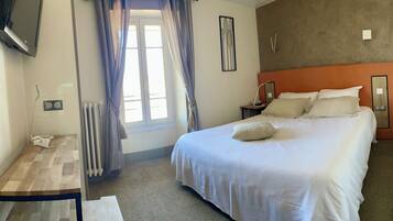 Una habitación de hotel con cama, mesita de noche y televisor montado en la pared.