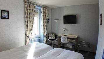 A hotel room with two beds, a desk with a chair, a television, and a window with curtains.