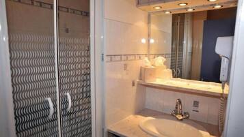 A bathroom with a glass shower enclosure, a sink with a mirror above it, and a towel dispenser.