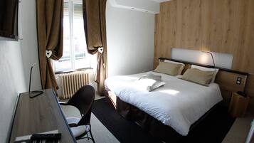 Ein Hotelzimmer mit einem Bett, einem Schreibtisch, einem Stuhl, einem Fenster mit Vorhängen und einer Holzwand.