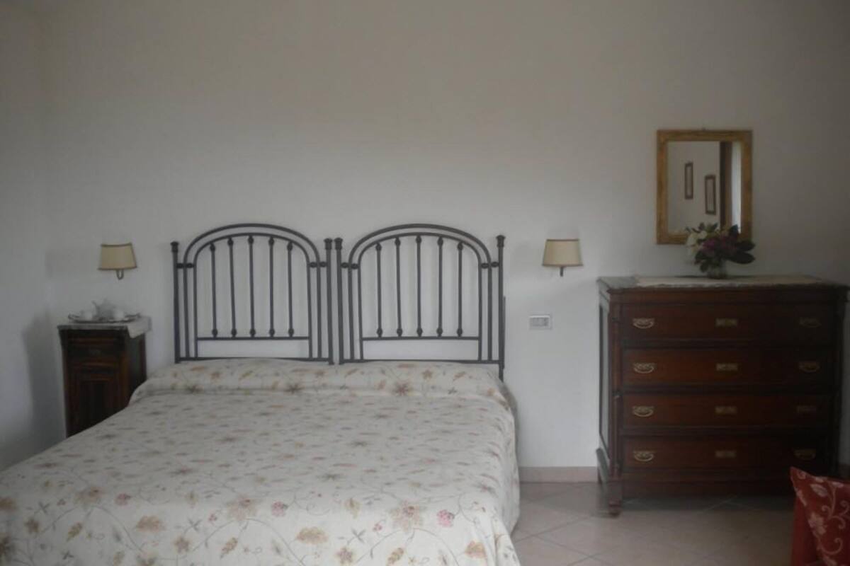 Une chambre à coucher comprenant un lit, deux lampes fixées au mur, une commode et un miroir.