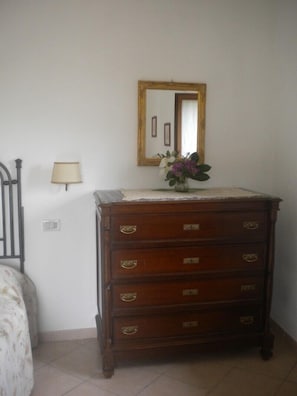 Een slaapkamer met een houten dressoir, een spiegel, een lamp en een bed met een bloemenbedekking.