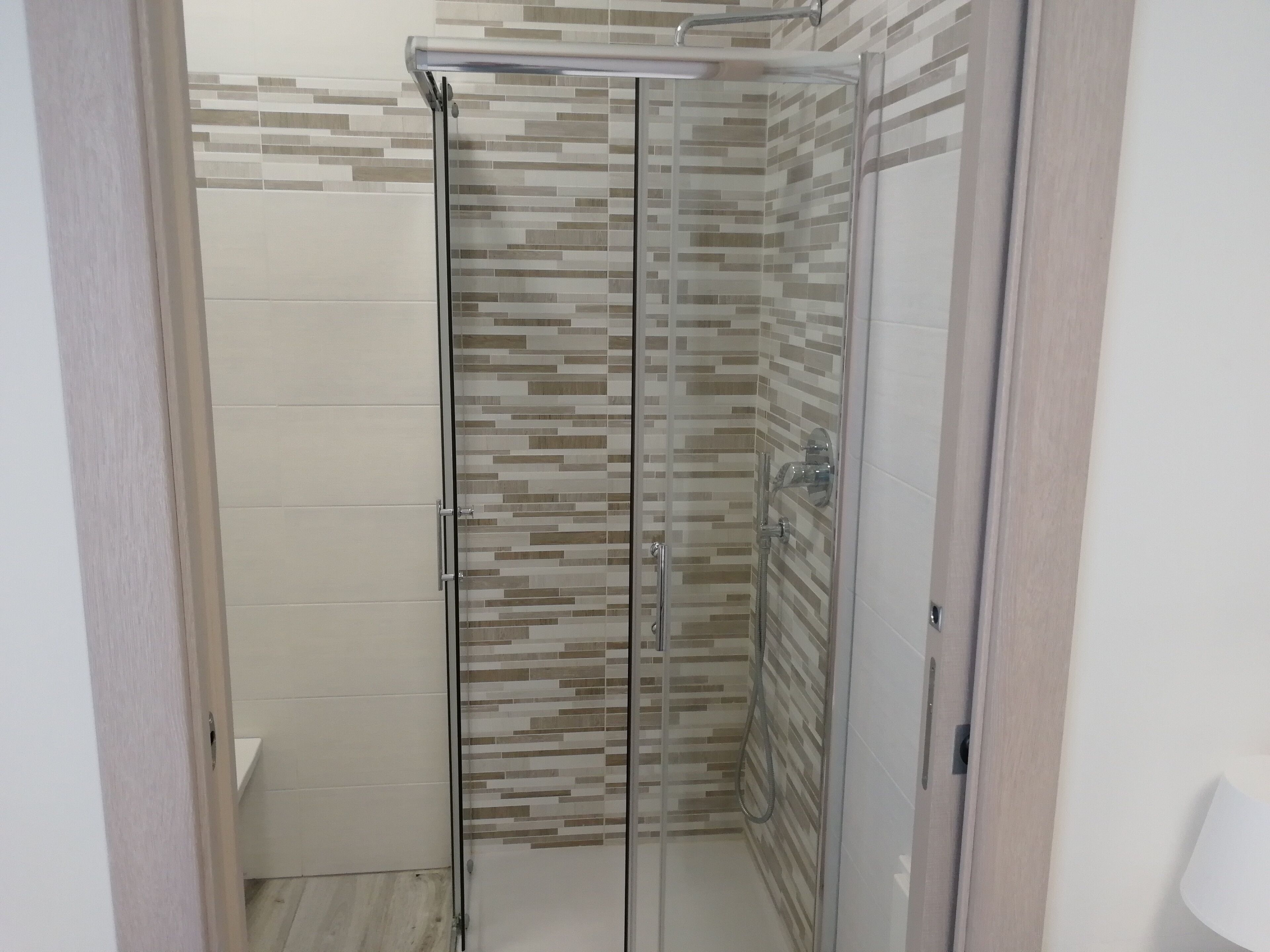 Una ducha con cerramiento de vidrio, pared de azulejos y suelo blanco.