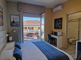 Camera d'albergo con un letto, una scrivania, una sedia, un condizionatore d'aria e vista del balcone esterno.