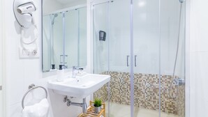 A modern bathroom with a glass-enclosed shower, a white sink, a hairdryer, and a small potted plant. - Pensión BUENPAS (San Sebastián)