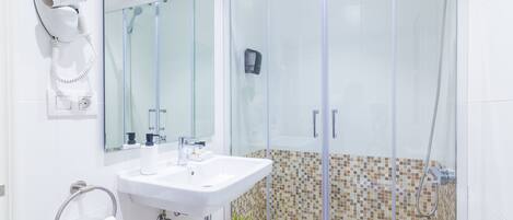 A modern bathroom with a glass-enclosed shower, a white sink, a hairdryer, and a small potted plant.
