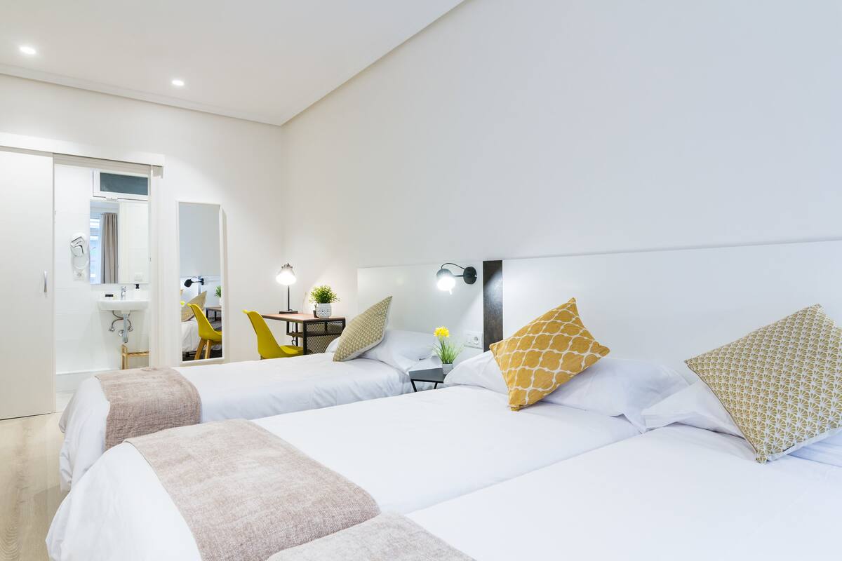 A hotel room with two beds, a bathroom, and a small sitting area with a chair and table.