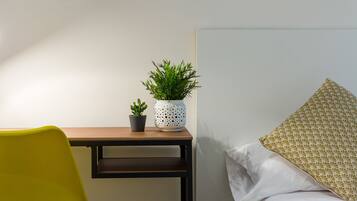 Een kamer met een bed, een bureau, een stoel en twee potplanten.