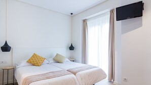 A modern hotel room with two beds, a flat-screen TV, and a large window with curtains. - Pensión BUENPAS (San Sebastián)