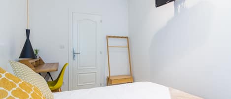 Un dormitorio con cama, escritorio, silla, televisor y puerta.