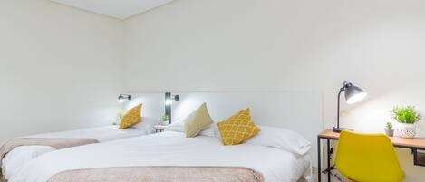 Un dormitorio con dos camas, un escritorio, una silla y una mesita de noche con una lámpara y una planta.