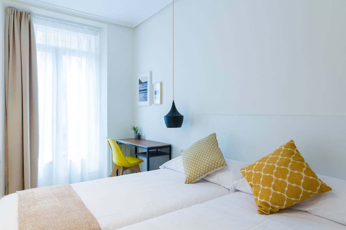 A hotel room with a bed, a desk, a chair, and a hanging light fixture.