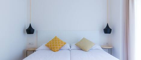 A double bed with two pillows, a bedside table, and two pendant lights.