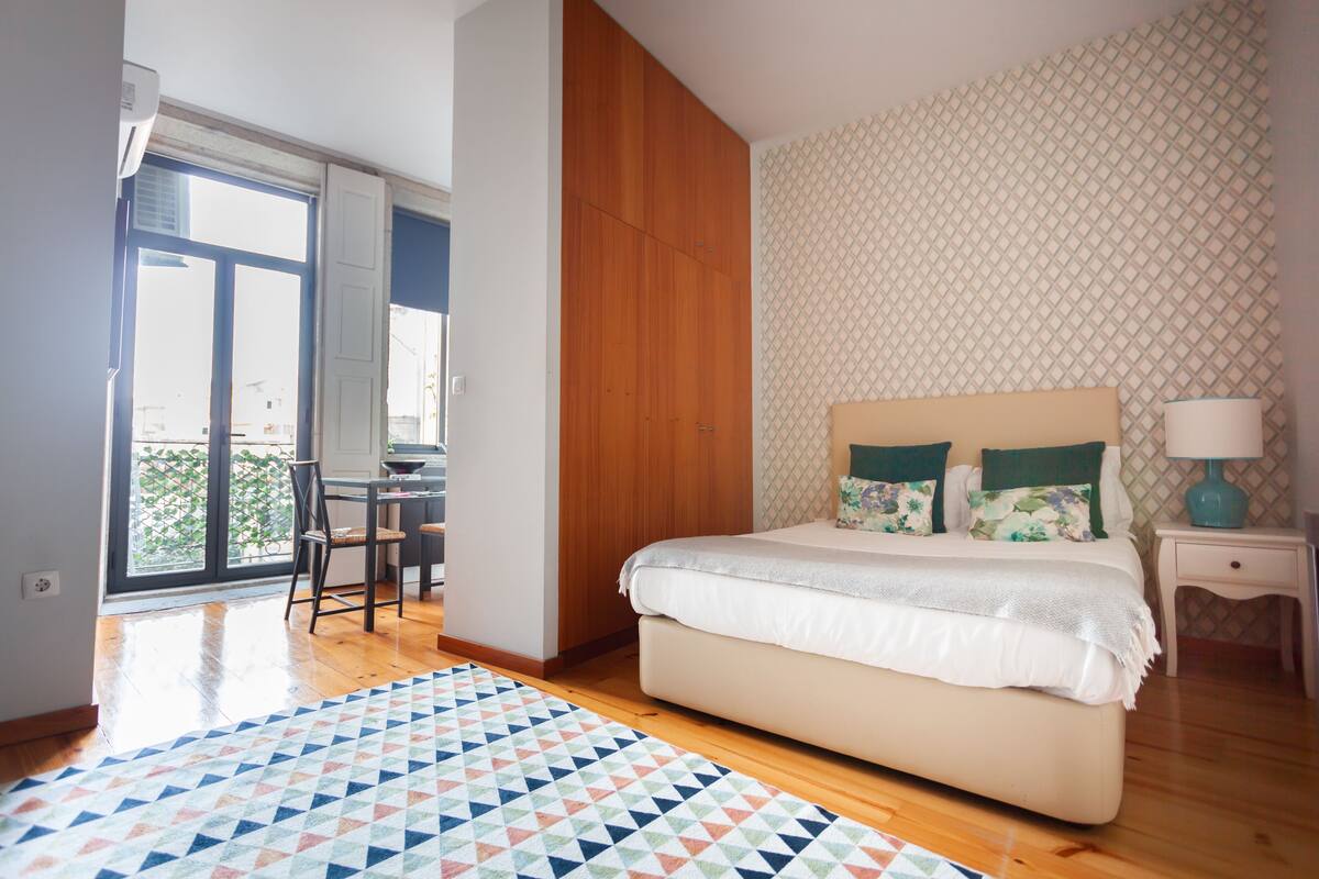 Une chambre avec un grand lit, une armoire en bois, un mur décoré d’un motif et une vue sur l’extérieur.