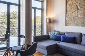 A modern living room with a glass table, dark grey sofa, and a stone wall artwork.