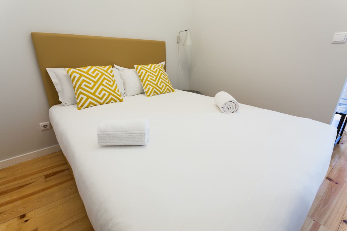 A neatly made bed with white and yellow patterned pillows, a folded white towel, and a wooden headboard.