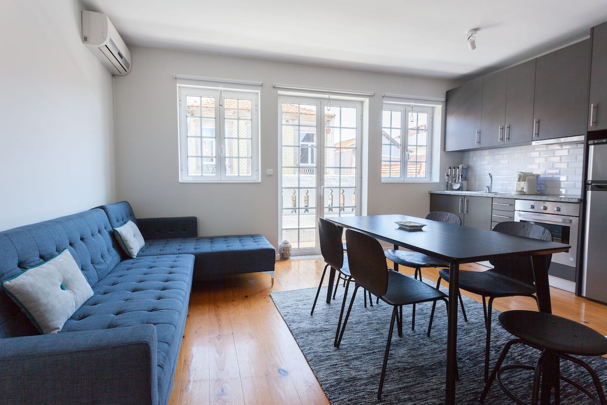 A modern kitchen with grey cabinets, a dining table with chairs, and a blue sofa with cushions.