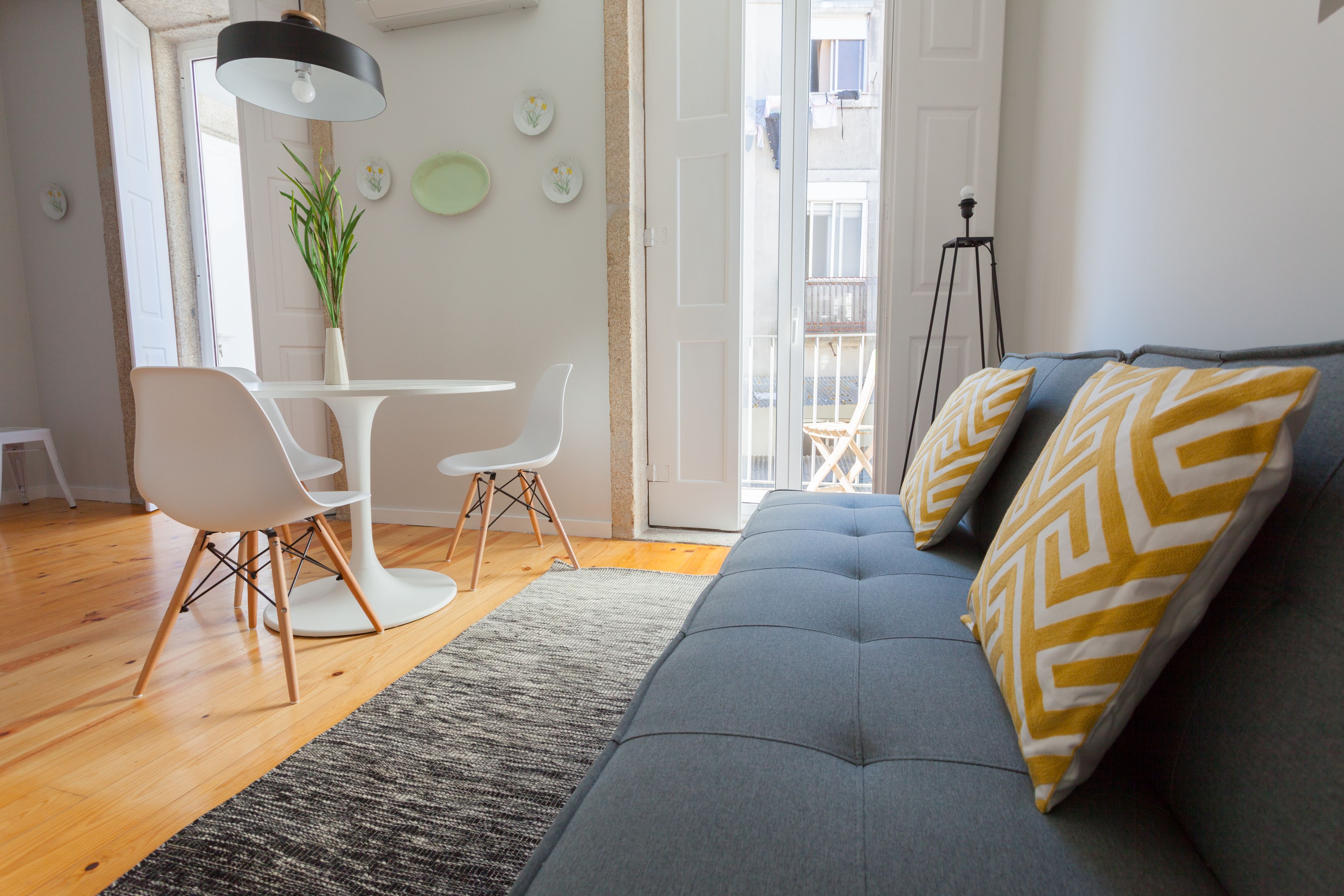 A modern living room with a grey sofa, white chairs, a small dining table, and a potted plant.