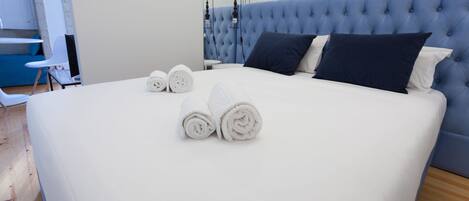 A neatly made bed with white linens and two rolled towels, a tufted headboard, and a small bedside table.