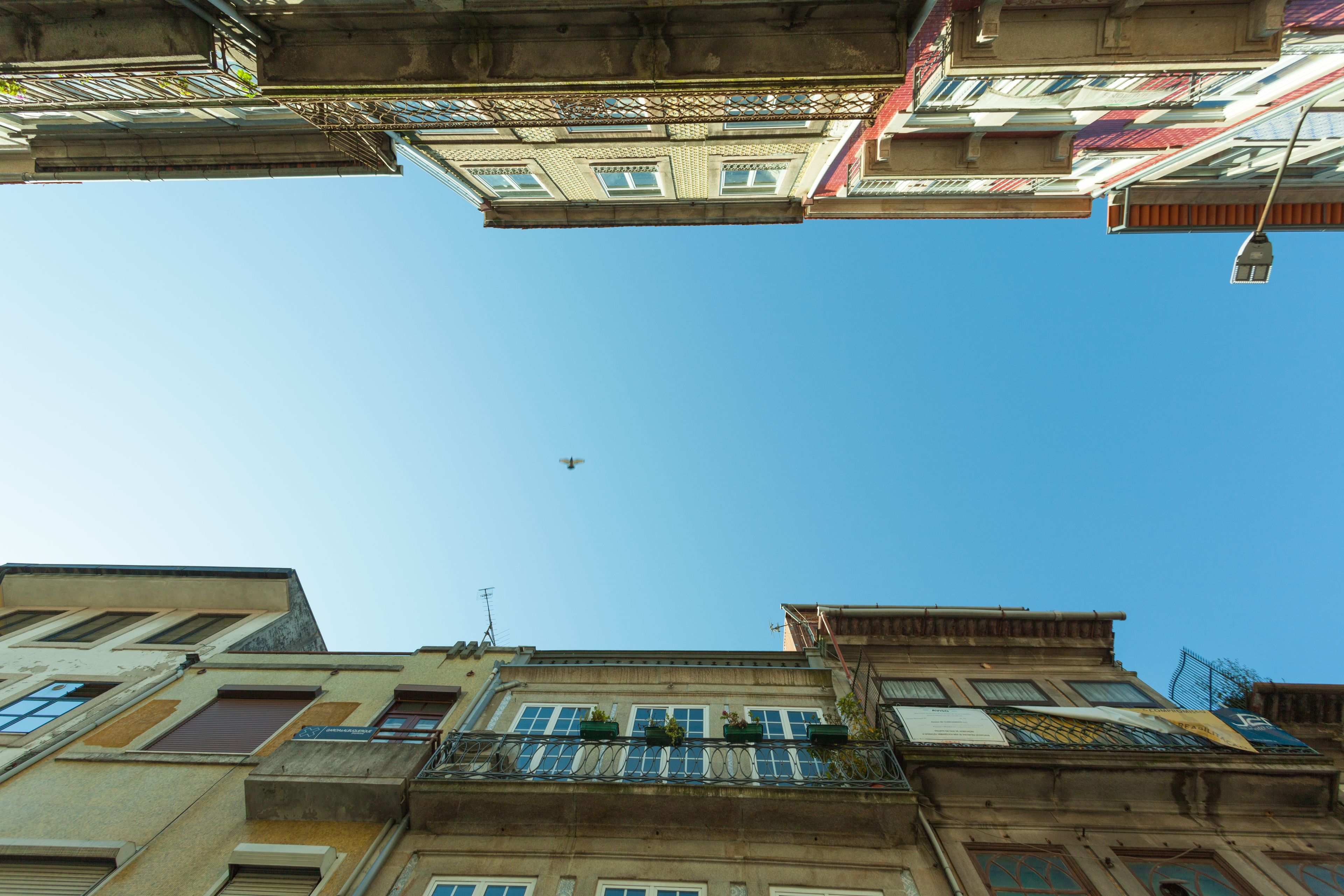 A view of a building with multiple balconies and windows, a clear sky, and a plane in the distance.