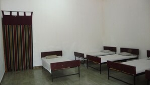 A dormitory room with four single beds, a curtain, and a tiled floor. - Palugaha Pilgrim Resort (Kataragama)
