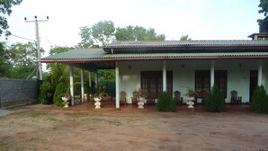 A two-story building with a covered porch, columns, and potted plants. - Palugaha Pilgrim Resort (Kataragama)
