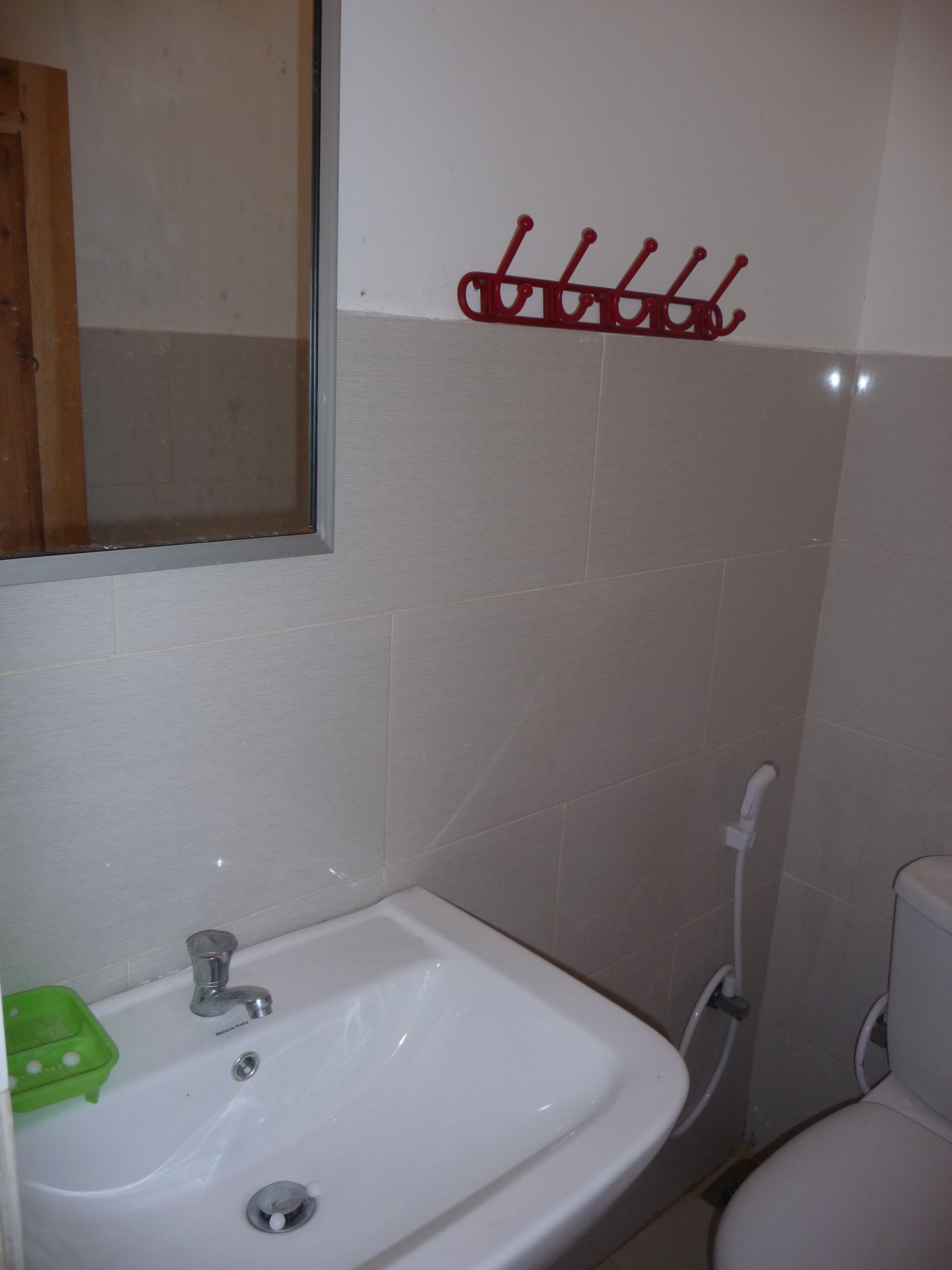 A bathroom with a white sink, a mirror, and a red towel rack.