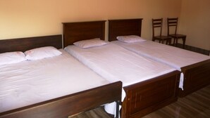 A room with three wooden beds aligned in a row, each with white linens. - Palugaha Pilgrim Resort (Kataragama)