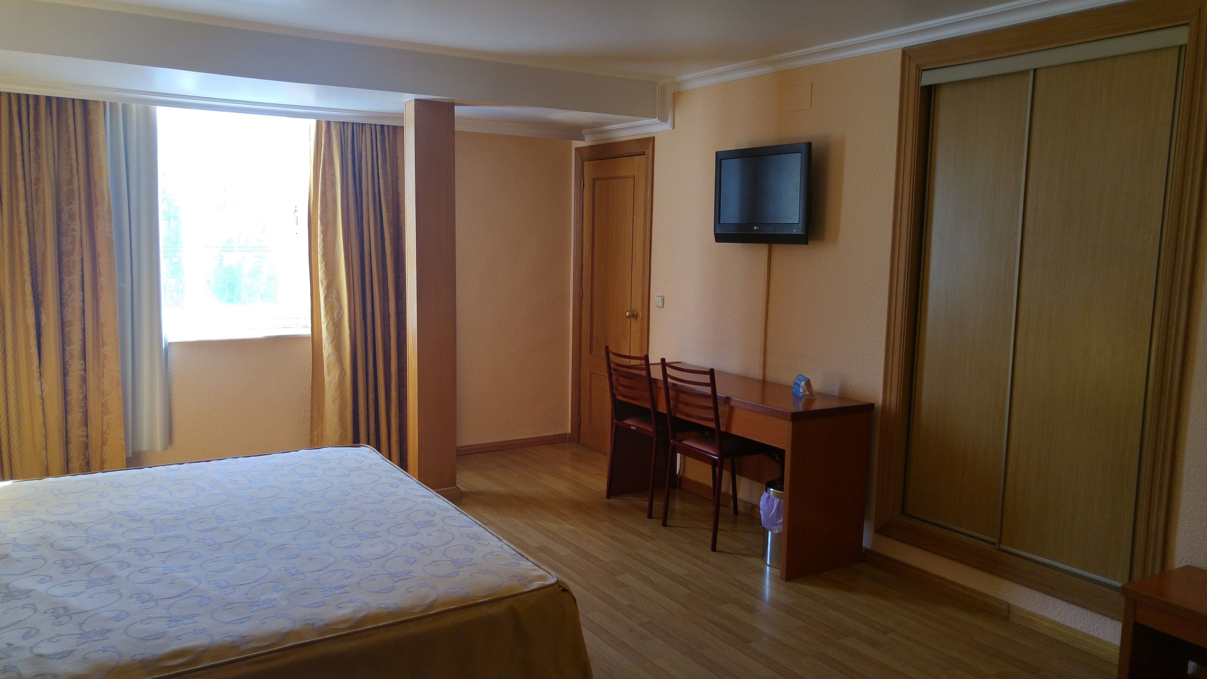 A hotel room with a bed, a desk with chairs, a television, and a wardrobe.