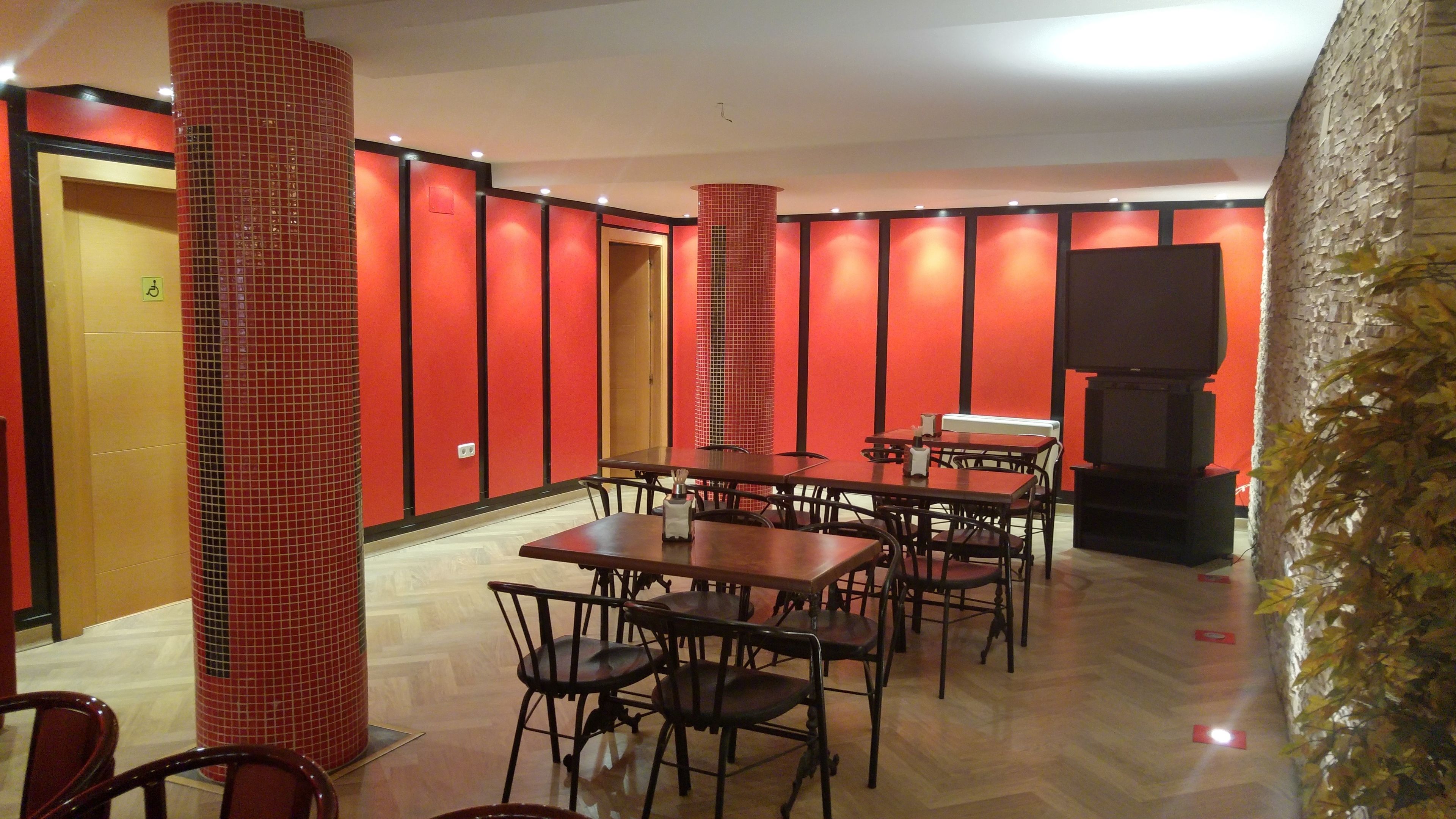 A restaurant with red walls, multiple tables and chairs, a pillar, and a television.
