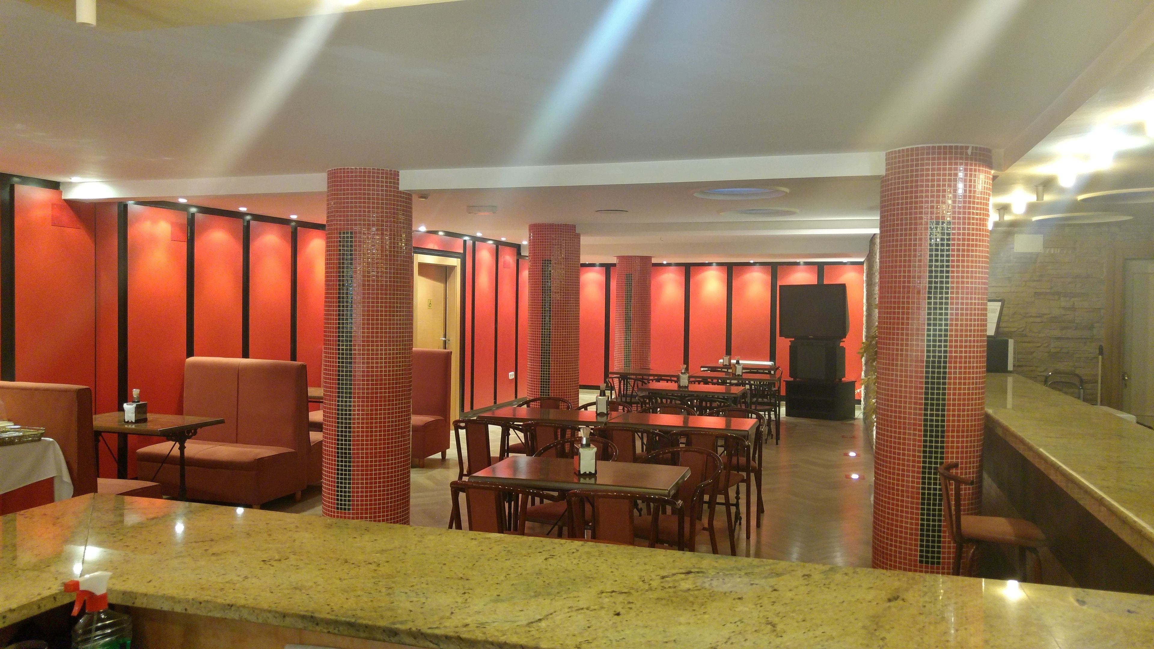A restaurant with red-tiled walls, multiple tables and chairs, and a television mounted on the wall.