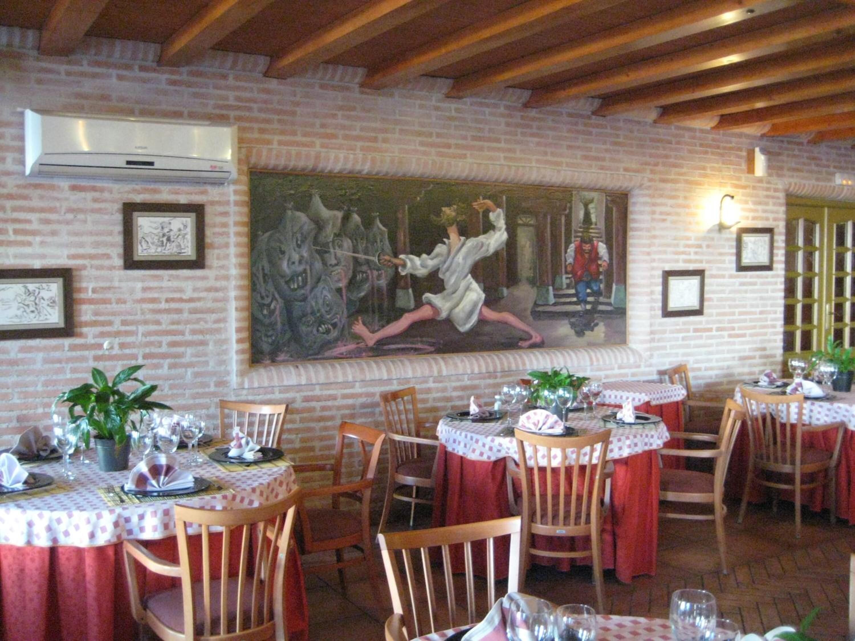 Un restaurant aux murs de briques, aux poutres apparentes et aux tables recouvertes de nappes rouges et ornées de verres à vin.
