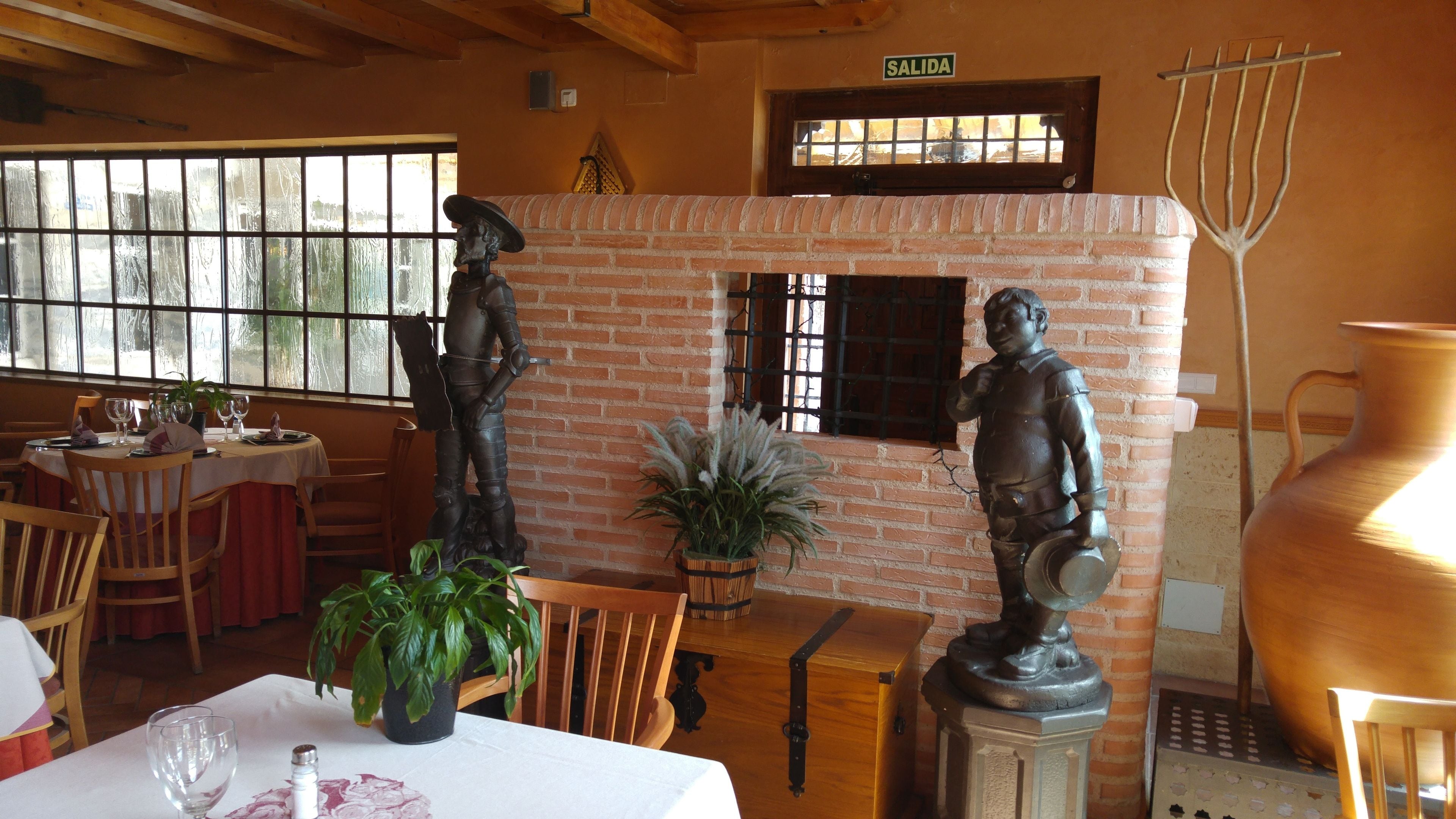 Interior de restaurante con paredes de ladrillo, chimenea y decoración rústica, incluyendo una estatua y una olla grande.